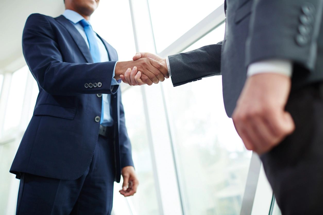 Two men in suits shaking hands over a window.